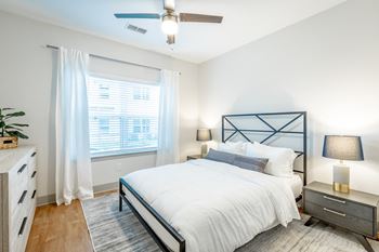 A bedroom with plank flooring, double window, and ceiling fan